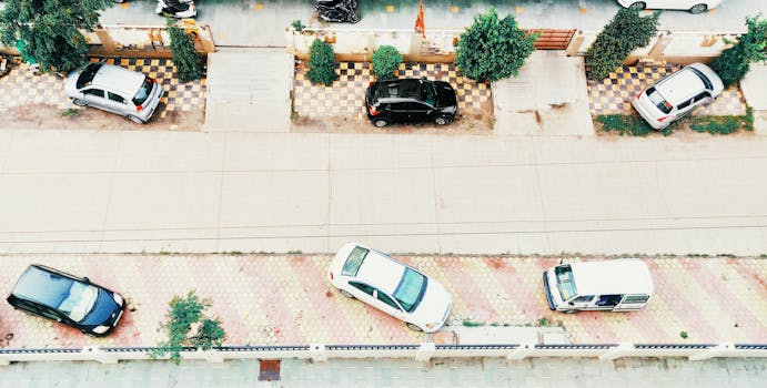 Aerial shot of an urban street in Indore, India, featuring parked cars along a tiled sidewalk and a quiet roadway.