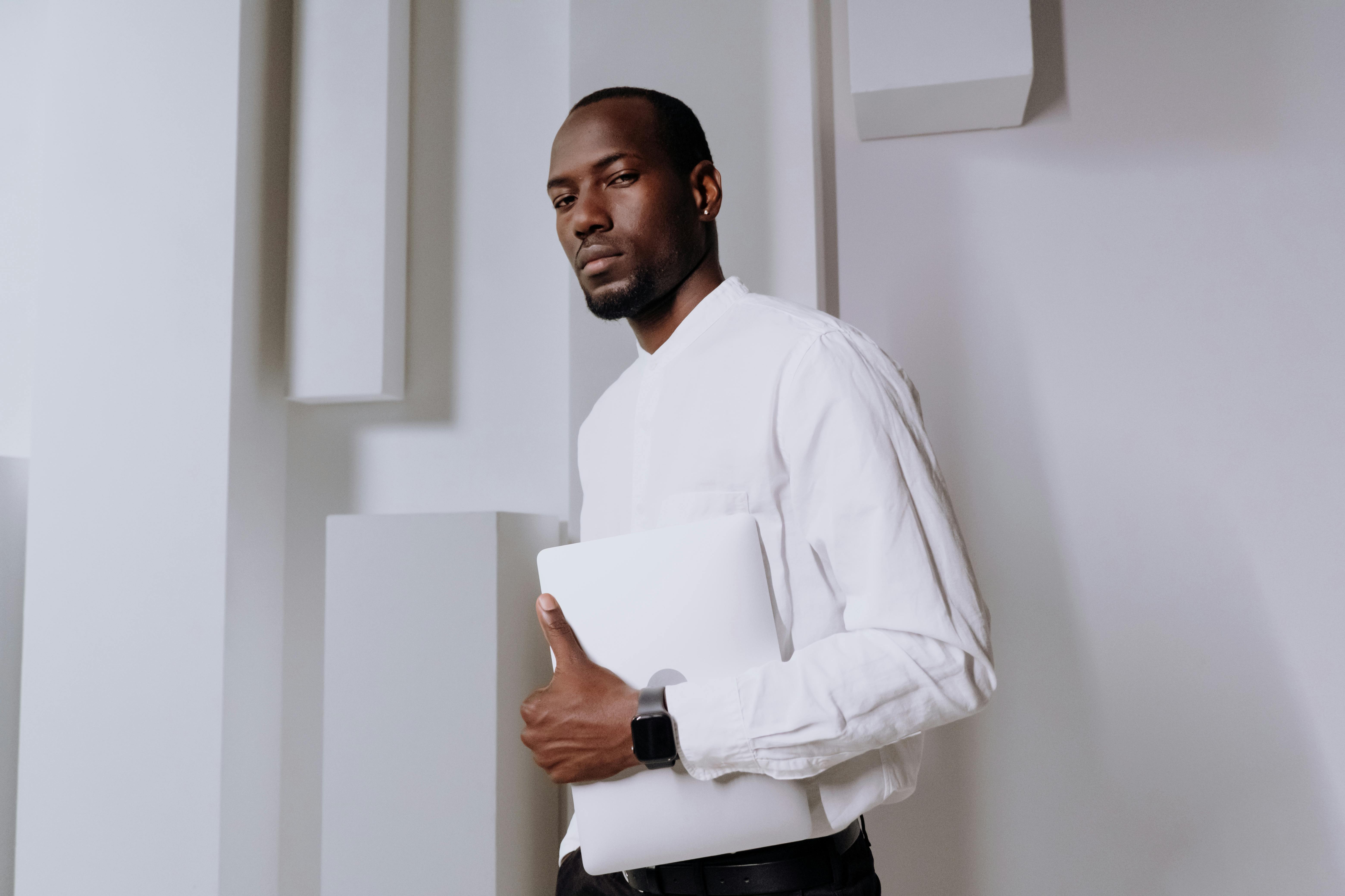 Businessman in a white shirt holding a laptop, wearing a smartwatch, in a modern office.