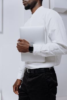 在现代办公环境中，一名身穿白衬衫、戴着智能手表的男子手持笔记本电脑