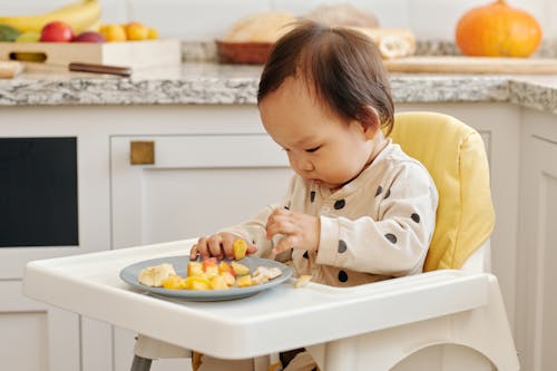 Free A Toddler Eating Fruits Sitting on the High Chair Stock Photo