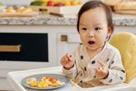 可爱的幼儿坐在室内的高脚椅上，享受健康的水果零食