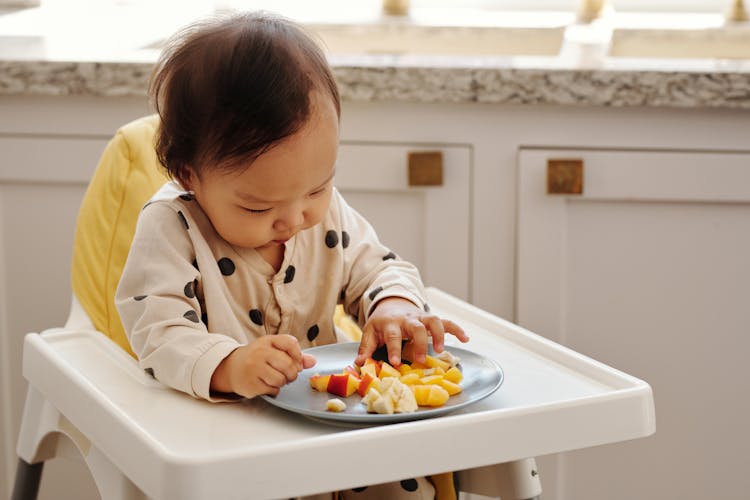 A Child Sitting On A Higher Chair Eating Fruits