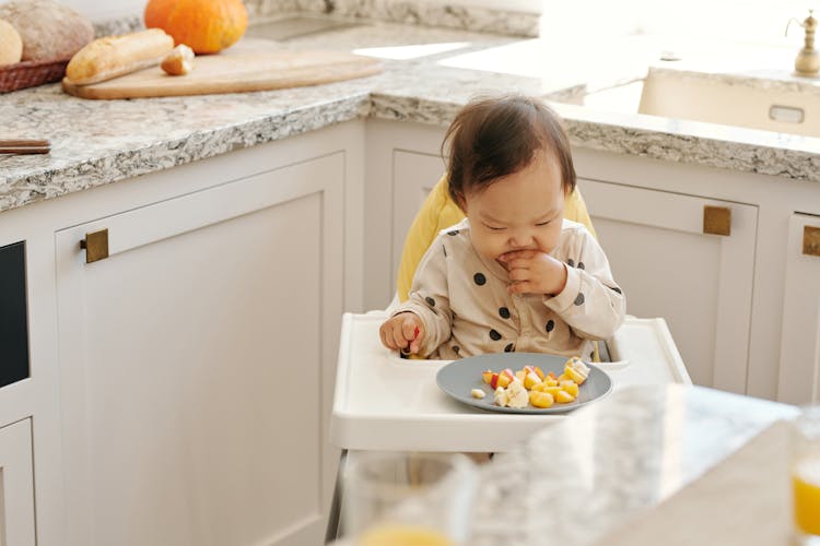 A Toddler Eating Fruits Sitting On A High Chair