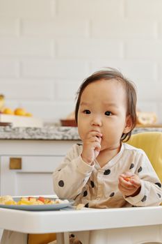 可爱的幼儿坐在高脚椅上吃水果，强调室内健康饮食