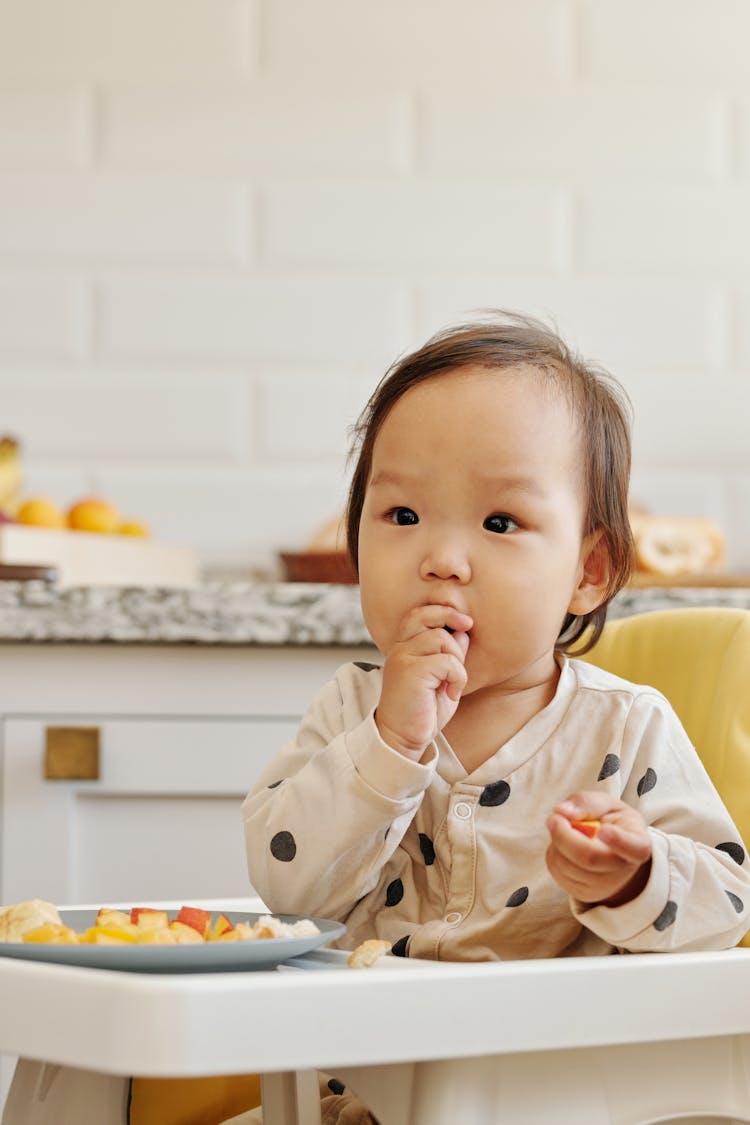 A Child In Polka Dots Clothes Eating Fruits