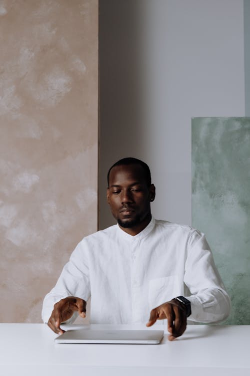 Man in White Dress Shirt Sitting Beside White Wall