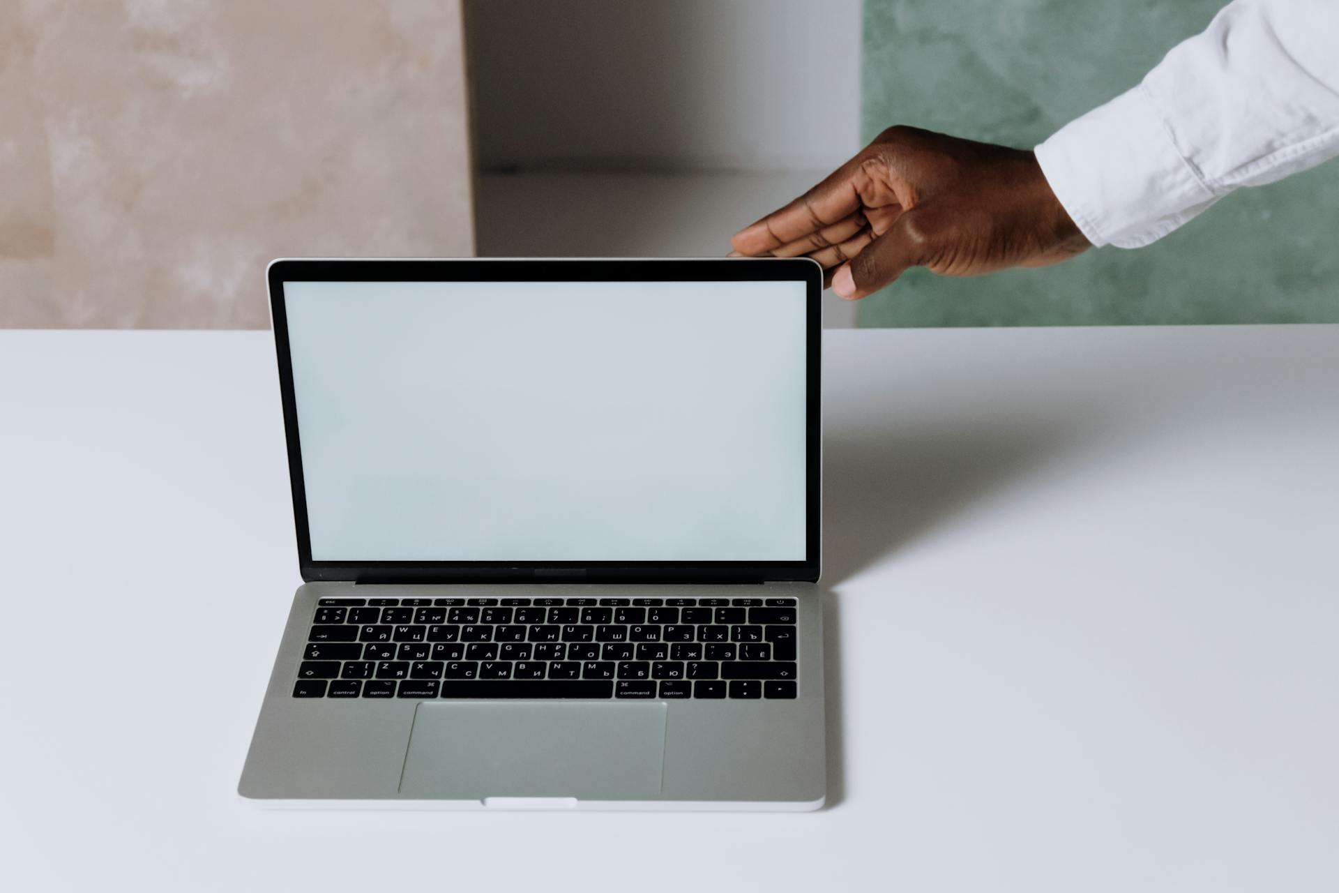 Laptop on a clean desk with a hand reaching towards it, perfect for business and technology themes.