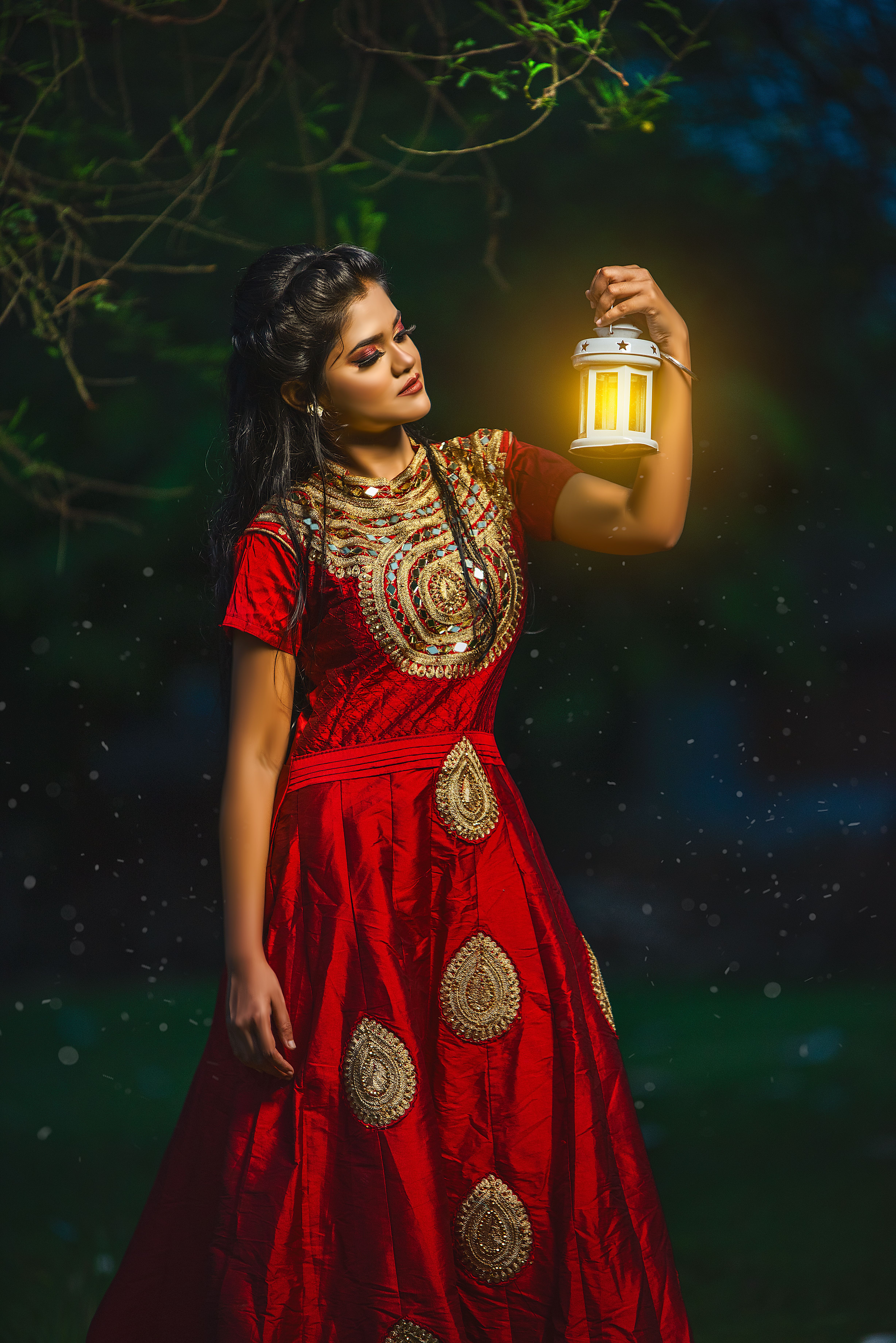 Beautiful woman in traditional red dress, holding a glowing lantern, standing outdoors at night.