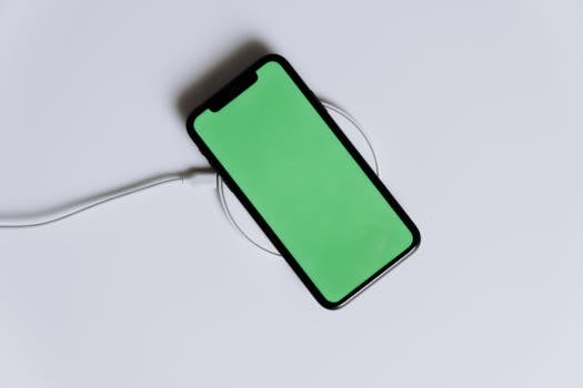 A minimalist smartphone with a green screen on a wireless charger, ideal for tech mockups.