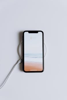 Minimalist smartphone on a wireless charger with a serene beach wallpaper.