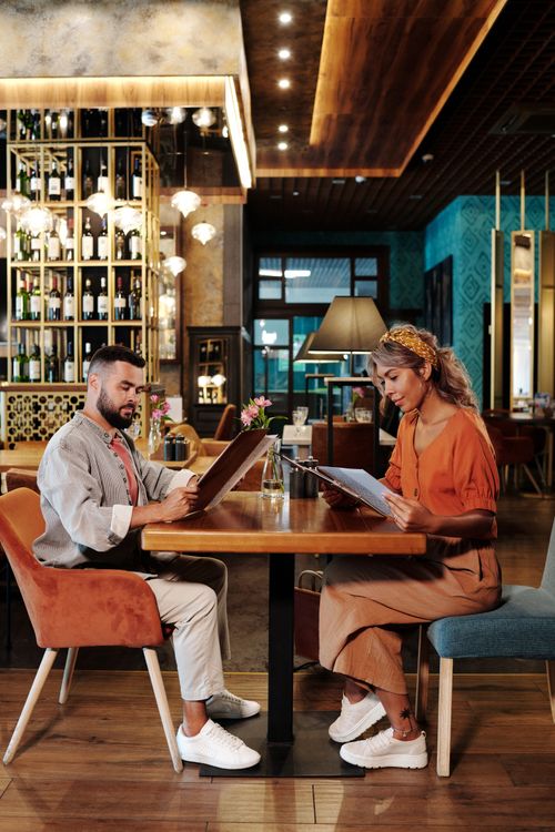 Free Two adults sit at a table in a chic restaurant, examining menus. Stock Photo