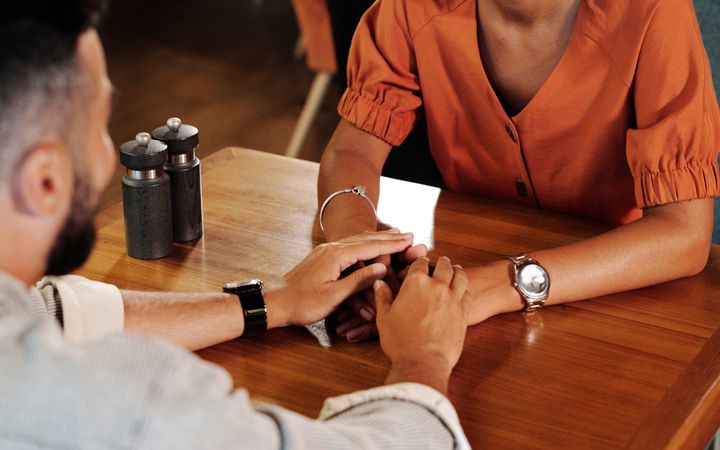 Couple holding hands and talking in a warm café setting, creating a romantic atmosphere.