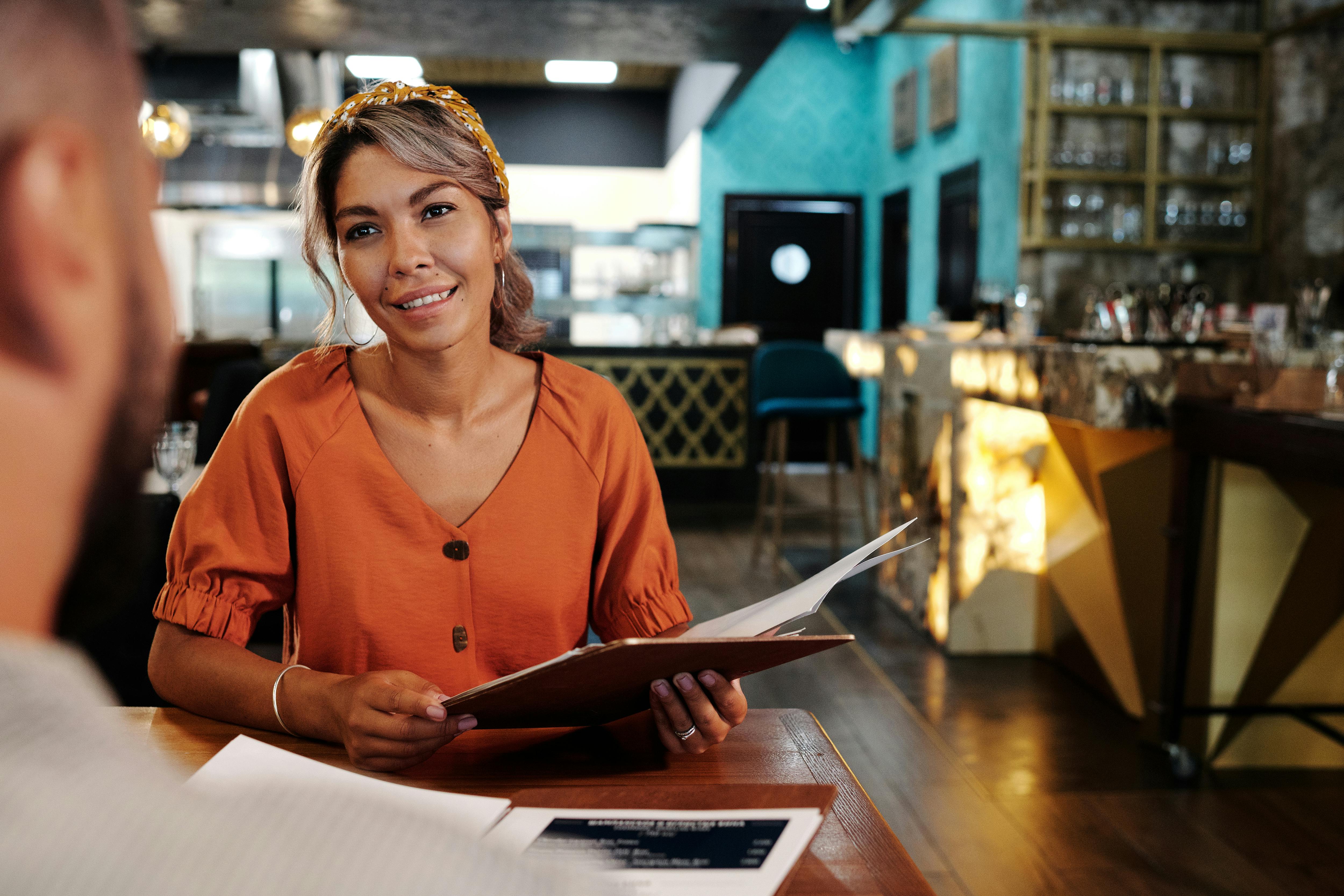 A woman in casual attire enjoying a conversation and browsing a menu in a stylish restaurant.