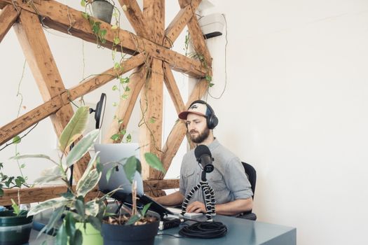 Man recording a podcast in a modern indoor studio with plants and wood panel decor.
