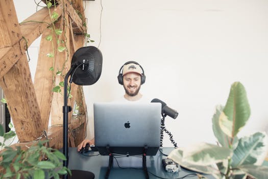 Man using laptop and microphone for podcasting in a modern setting.