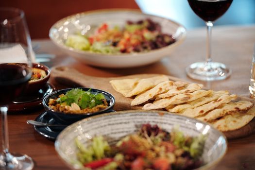 A close-up of a gourmet meal with fresh salad, bread, and red wine on a table.