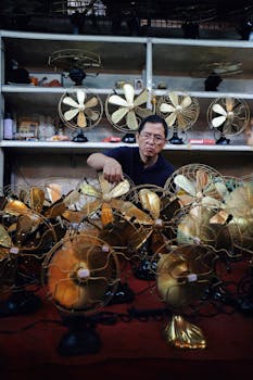 Man organizes vintage fans at an indoor antique shop stand, showcasing retro merchandise.
