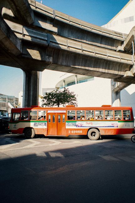 Bus full of people moving on asphalt road on station under overhead passage in sunny day