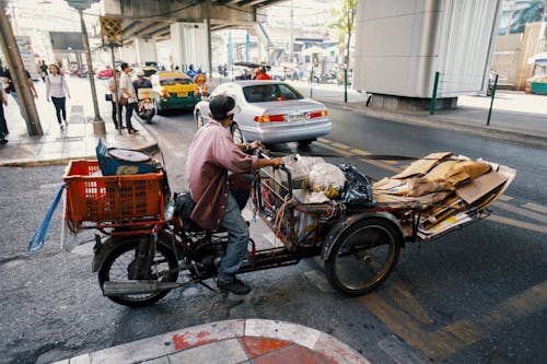 Full body side view of ethnic man carrying packages and cartons on tricycle while crossing asphalt road