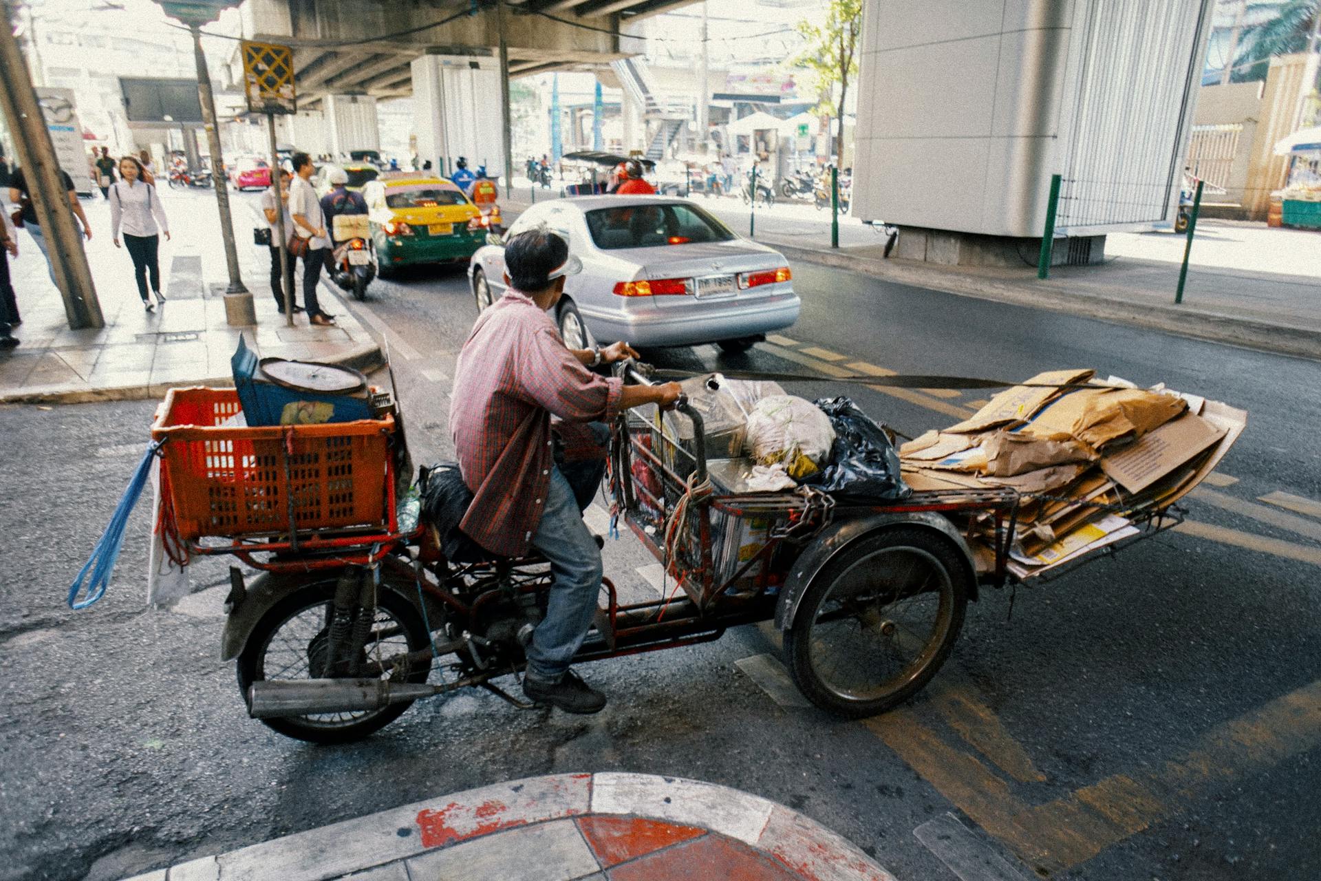 Full body side view of ethnic man carrying packages and cartons on tricycle while crossing asphalt road