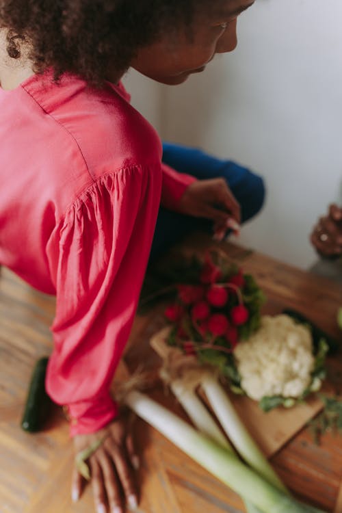 Person in Red Long Sleeves Shirt Sitting on Brown Wooden Table Beside Fresh Vegetables