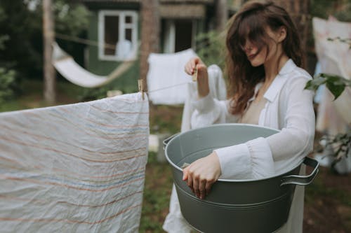 Free Woman in White Long Sleeves Shirt Putting the Clothes in the Bucket Stock Photo