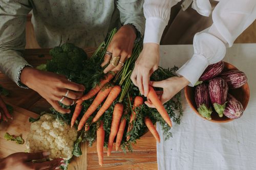 Free Diverse hands assorting fresh vegetables like carrots and eggplants on a rustic wooden table. Stock Photo