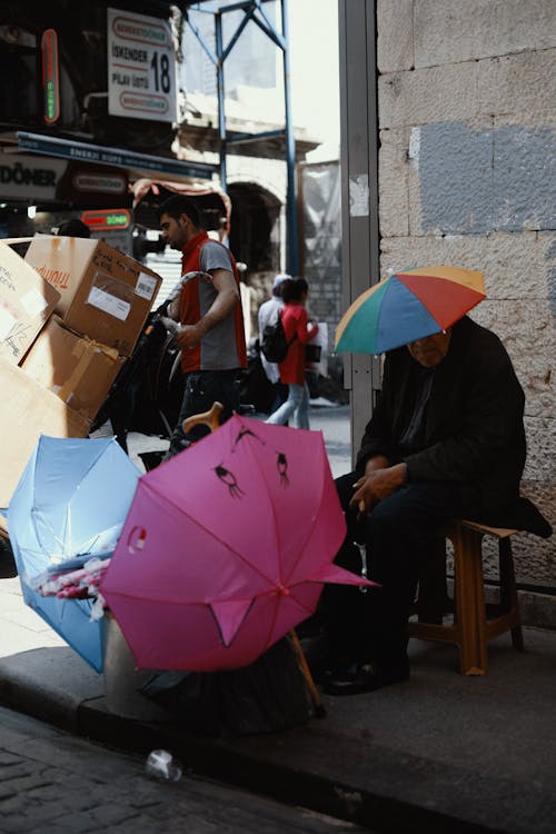 Old man in colorful umbrella on head selling umbrellas