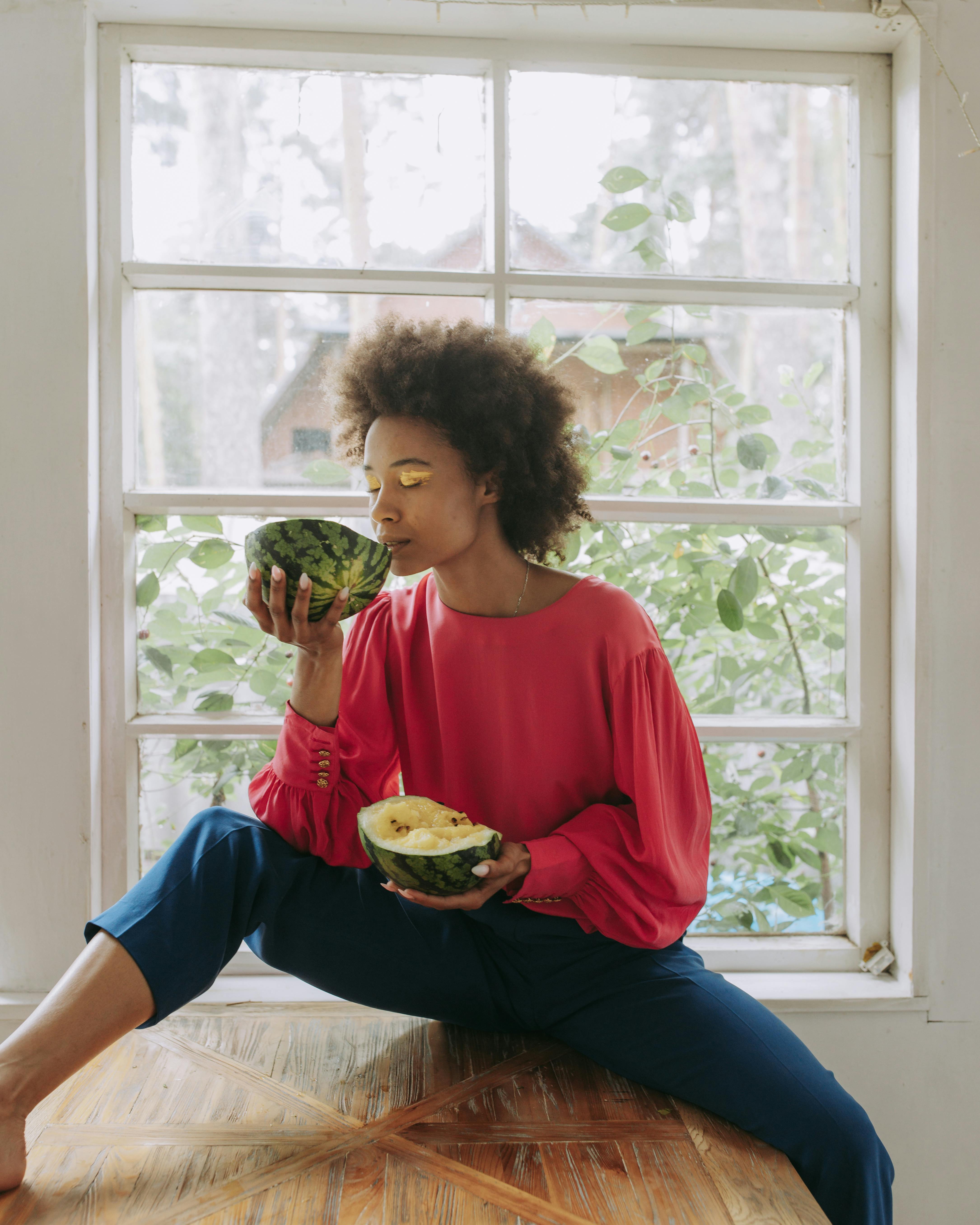 Woman sitting by window, savoring fresh watermelon indoors.