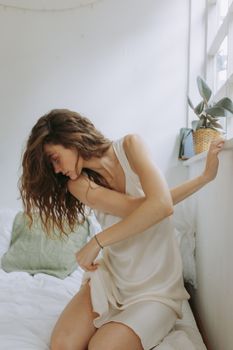 Young woman in soft light bedroom setting enjoying a serene morning.