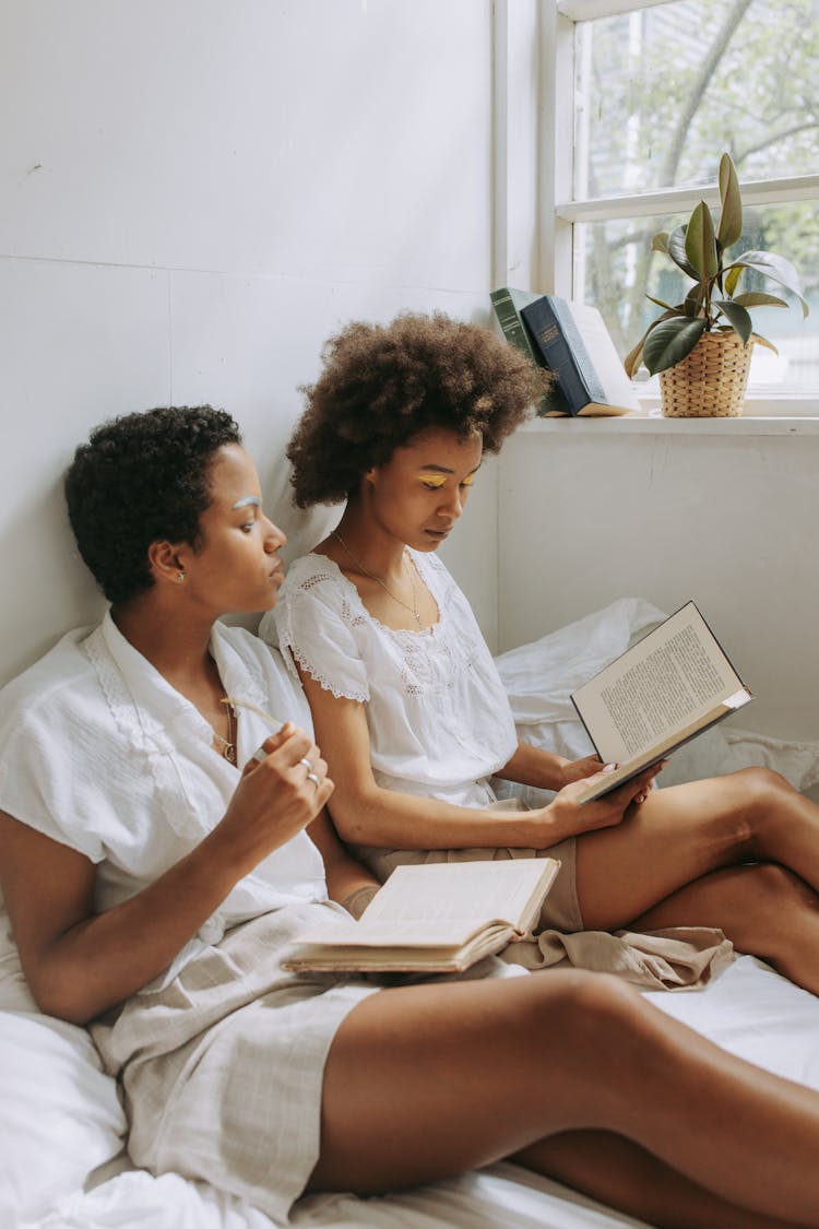 Women Sitting On The Bed While Reading Books