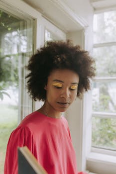 Beautiful portrait of a woman with afro hair and gold eyeshadow in a pink shirt, exuding elegance and style.