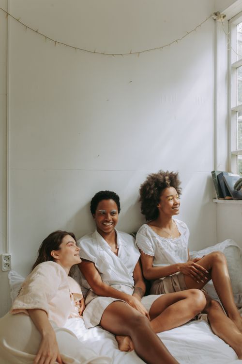 Free Three diverse women sitting together indoors, smiling and enjoying a relaxed moment by the window. Stock Photo