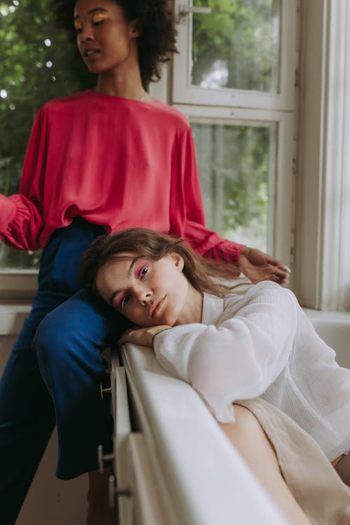 Free Woman in White Long Sleeve Shirt Reclining On A Couch Beside A Woman In Red Long Sleeve Shirt Stock Photo