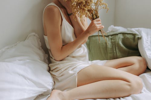 Free Woman in White Sleepwear Sitting on Bed Holding Bunch of Flowers Stock Photo