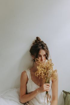 A young woman in minimalistic attire holding dried flowers, capturing a serene and introspective atmosphere.
