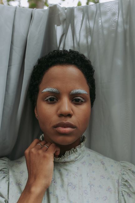 Elegant portrait of a woman with unique colored eyebrows in a vintage-style setting.