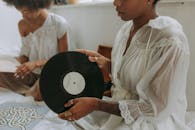 两名女子身穿白色休闲连衣裙，在室内欣赏黑胶唱片