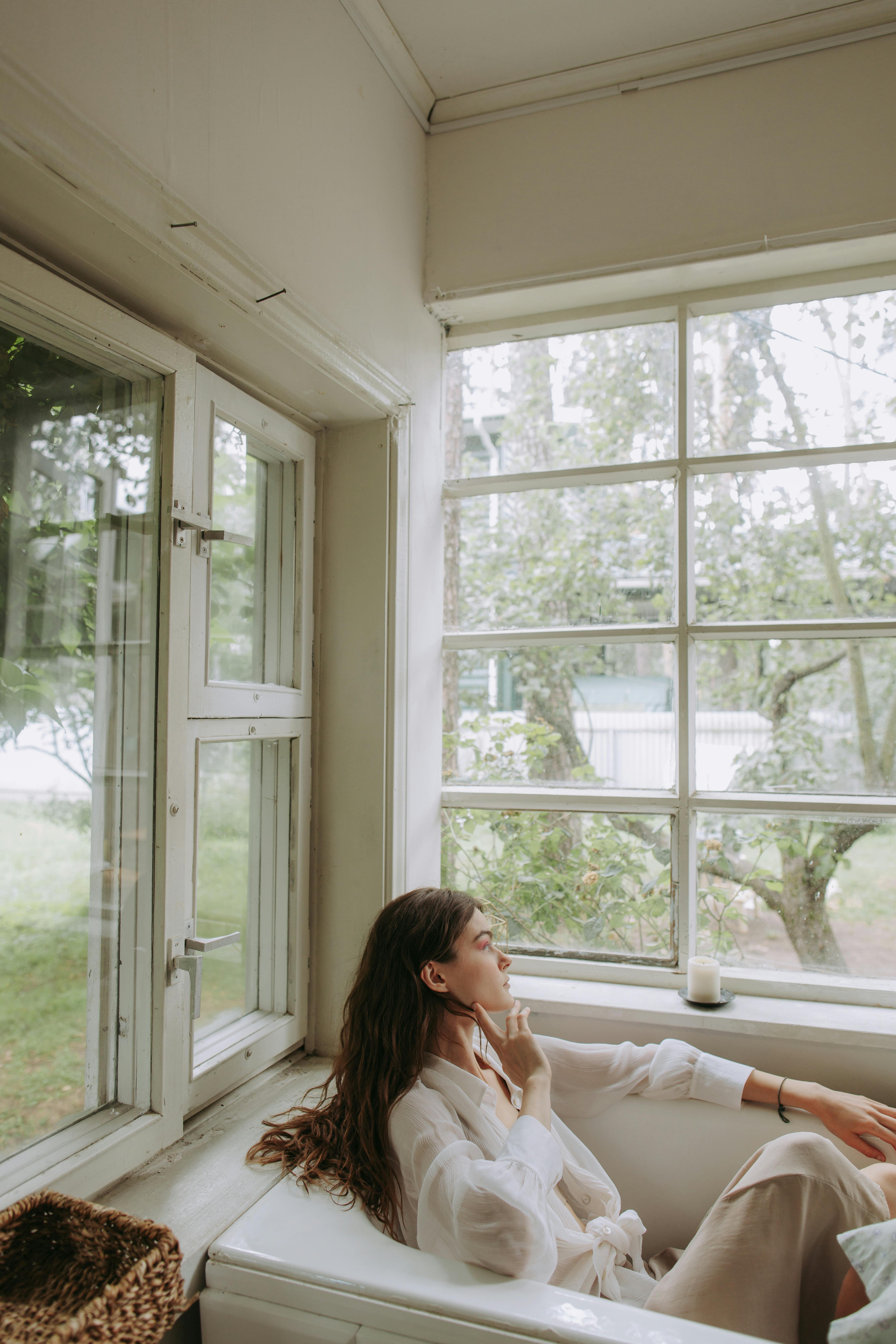 woman in white long sleeve shirt sitting on bed near window