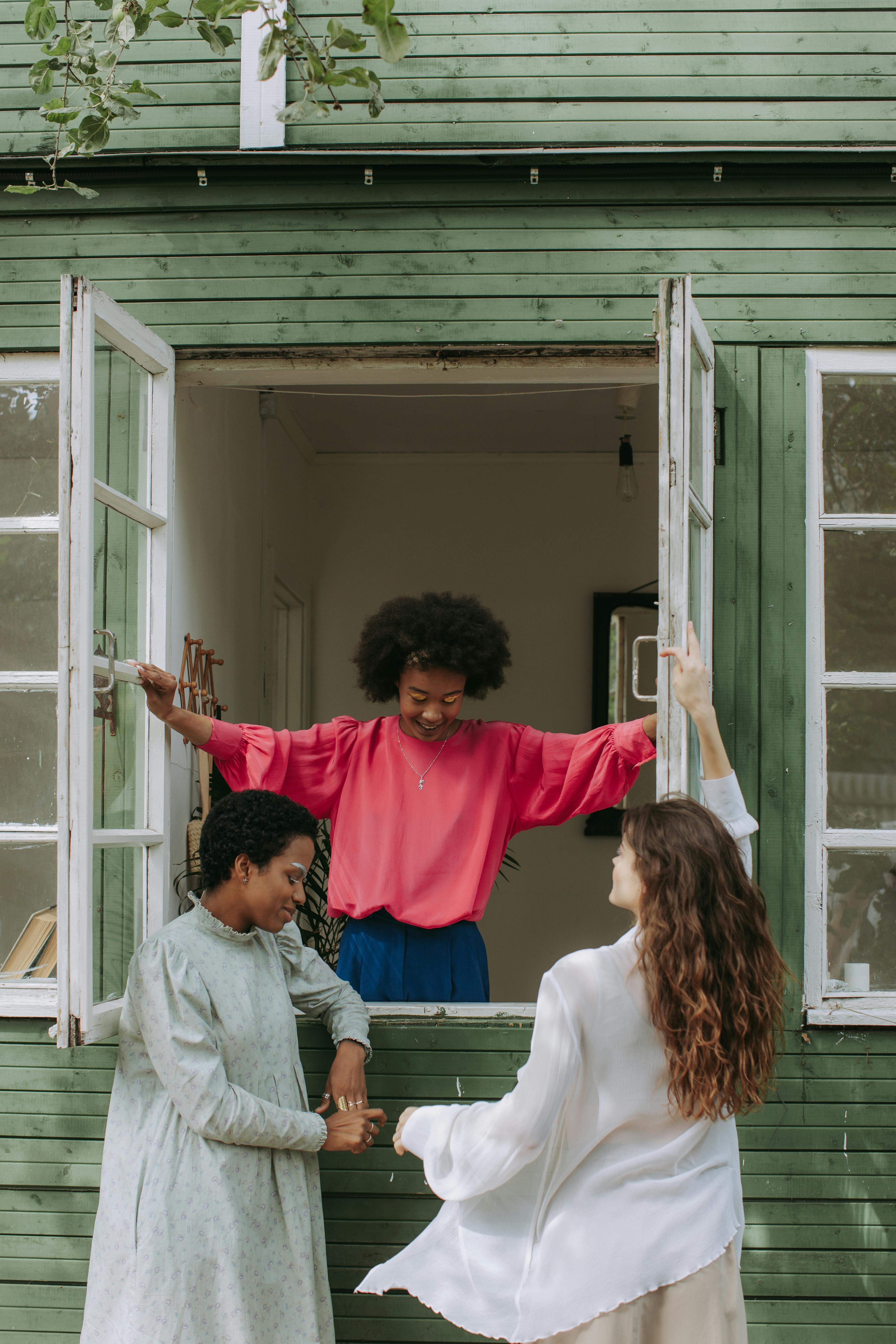 2 women in red long sleeve shirt standing beside white wooden framed glass window