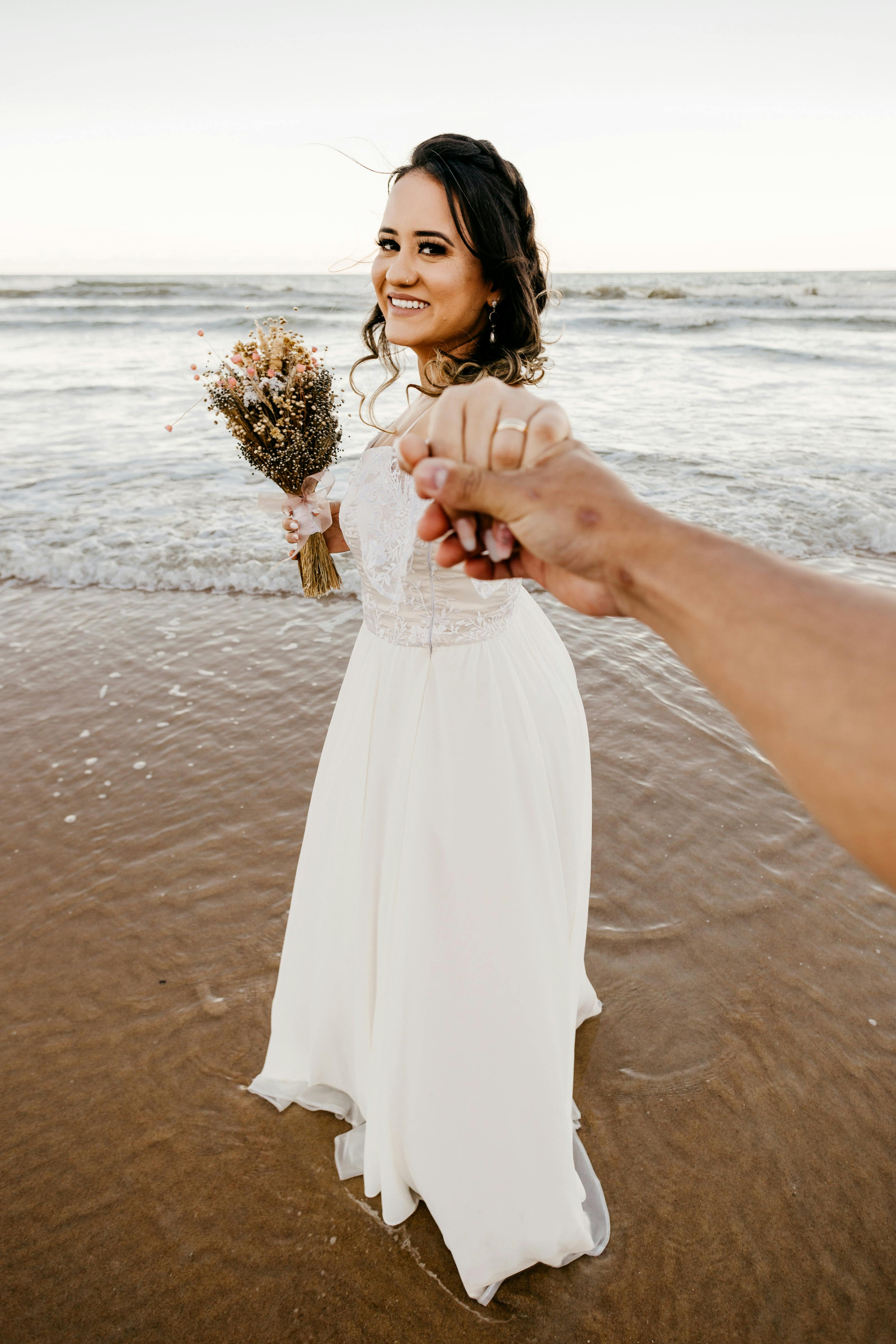 bride in white dress standing on sandy beach