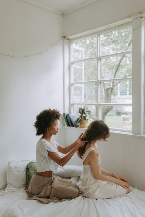 Free Two women share a tender moment sitting by a window in a serene, sunlit room. Stock Photo