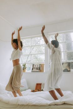 两个女人在阳光明媚、有大窗户的房间里，快乐地在床上跳舞