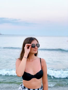 Young woman in bikini with sunglasses at Eforie Nord beach during a serene summer sunset.
