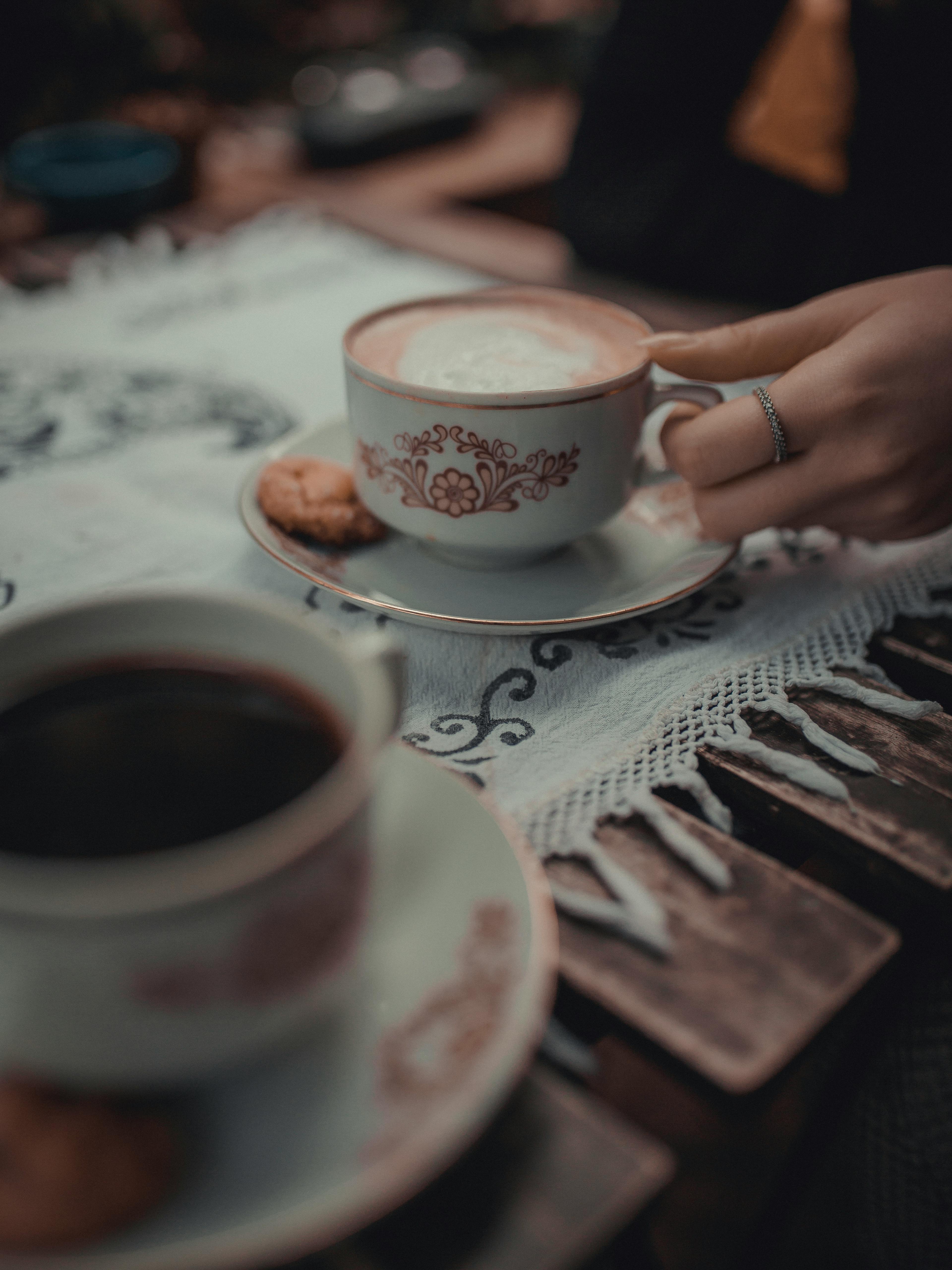 A detailed capture of a hand holding a ceramic coffee cup on a lace-covered table in Istanbul.