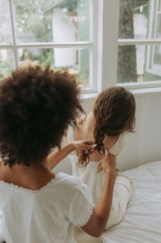 一名女子在室内靠窗为另一名女子编发，营造出舒适的氛围