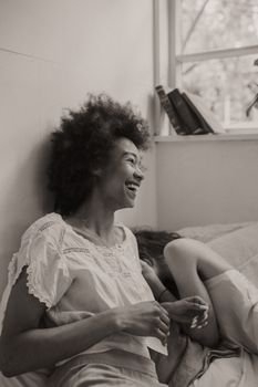 在这张单色照片中，一位留着非洲式发型的女人笑着在床上分享快乐的时刻