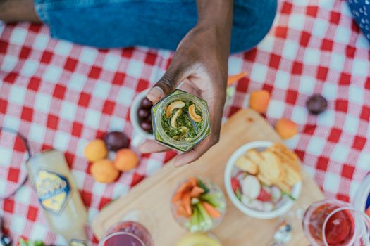 Close-up of a hand holding a jar of cashew pesto on a picnic blanket, highlighting a summer outdoor vibe.