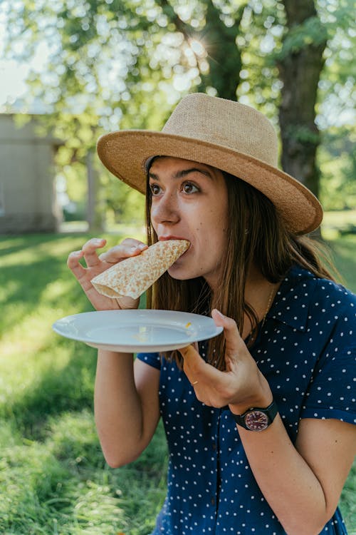 Woman in Blue and White Polka Dot Dress Eating a Flatbread