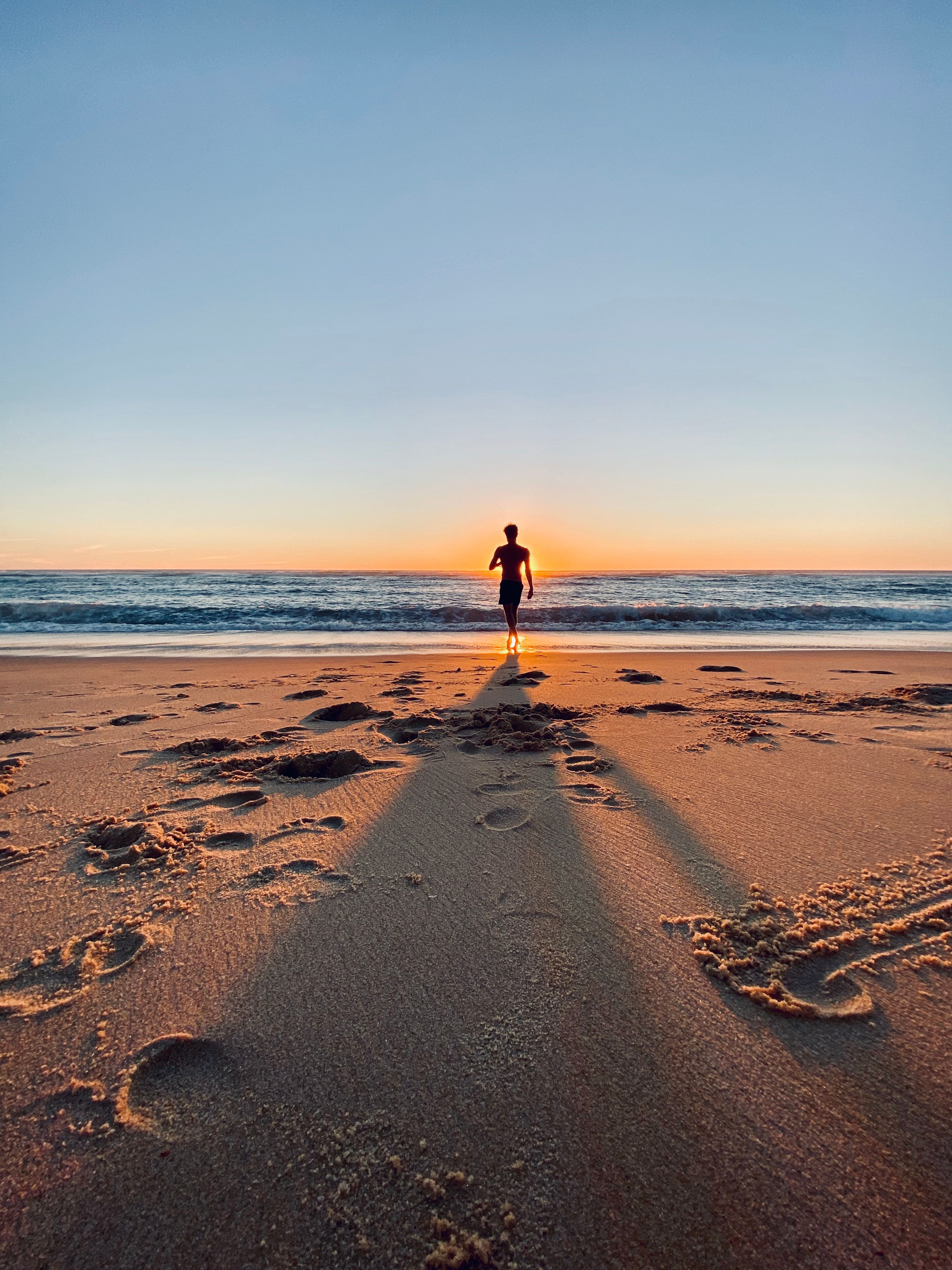 A person walks along Vielle-Saint-Girons beach in France, casting long shadows at sunset.
